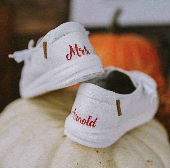 Back heels of white Hey Dude shoes with Mrs. Arnold painted on them. Shoes are sitting on a pumpkin for a fall wedding.