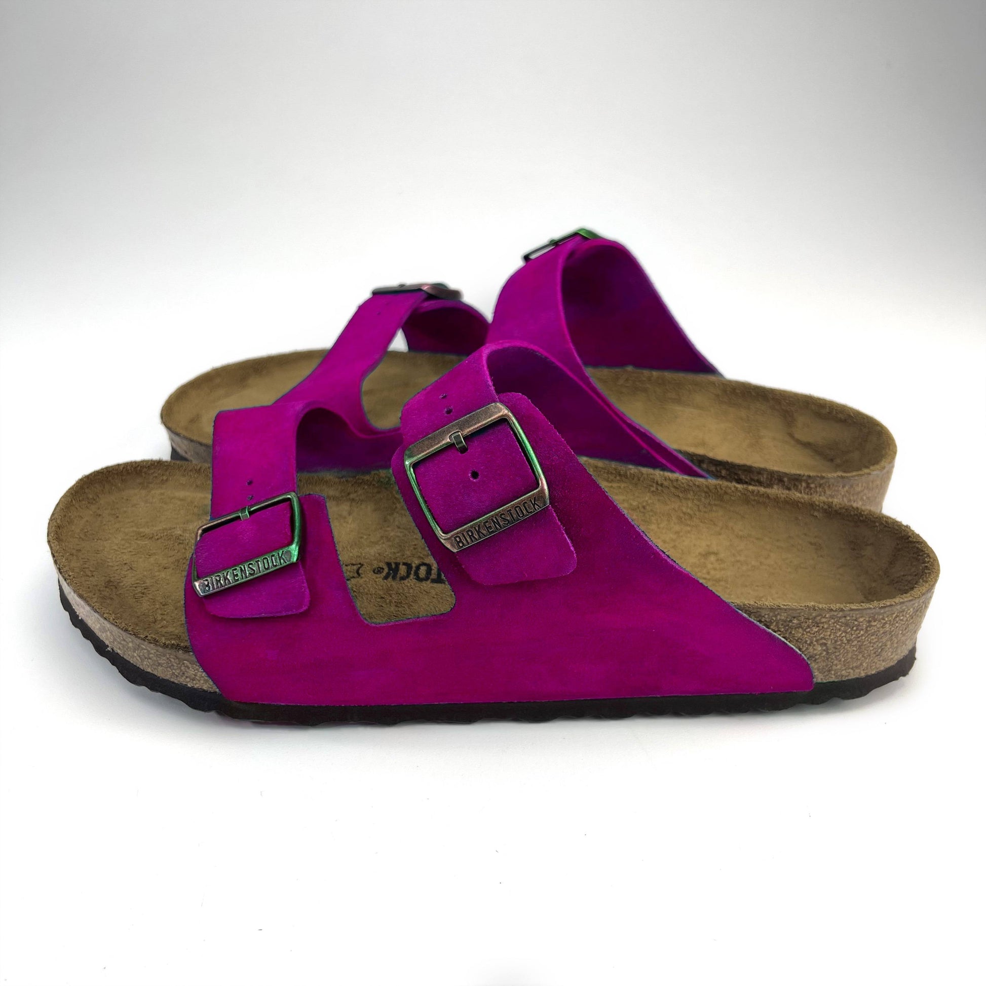 side view of Fuchsia Magenta Birkenstock Sandals with copper buckles on a white back floor