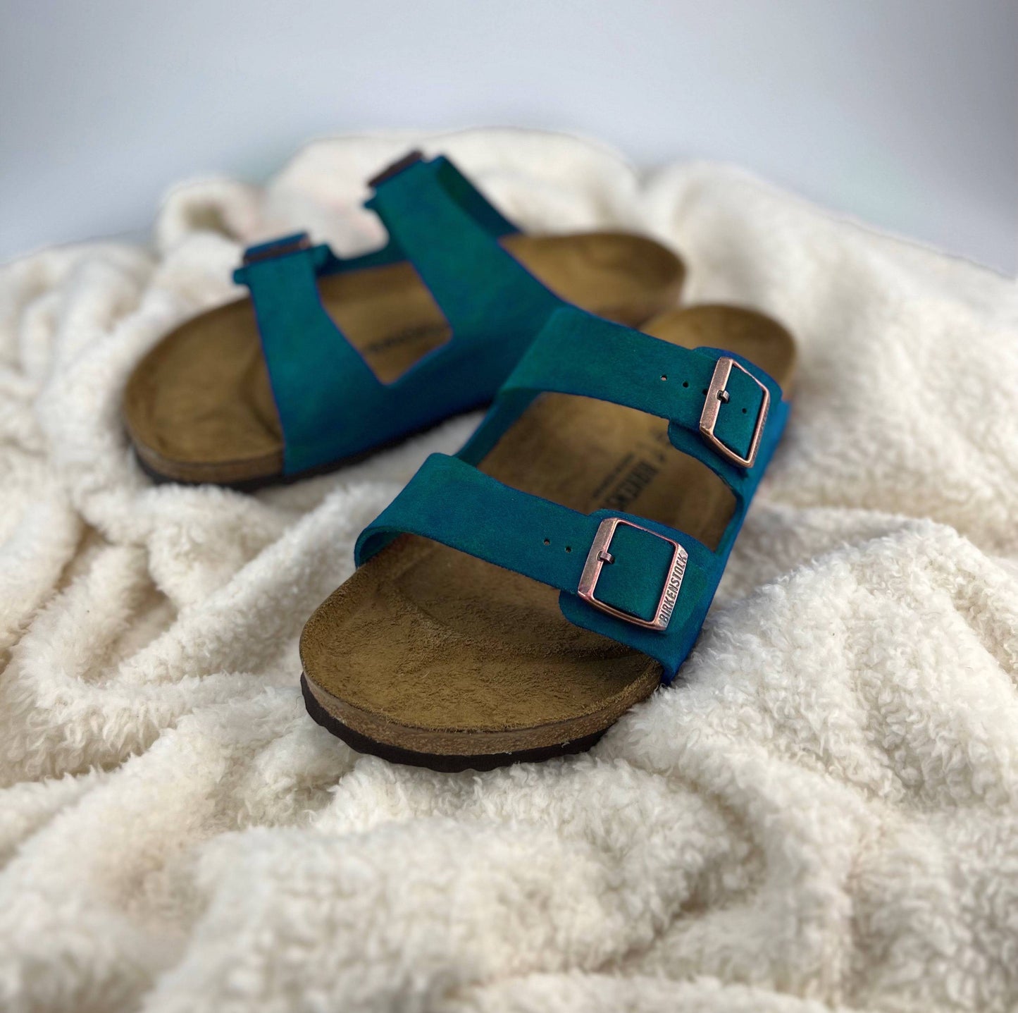 Teal Birkenstock Sandals with 2 straps & copper buckles on a white sherpa blanket