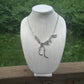 Silver Tyrannosaurus Rex Bones necklace on a outdoor display with greenery in background